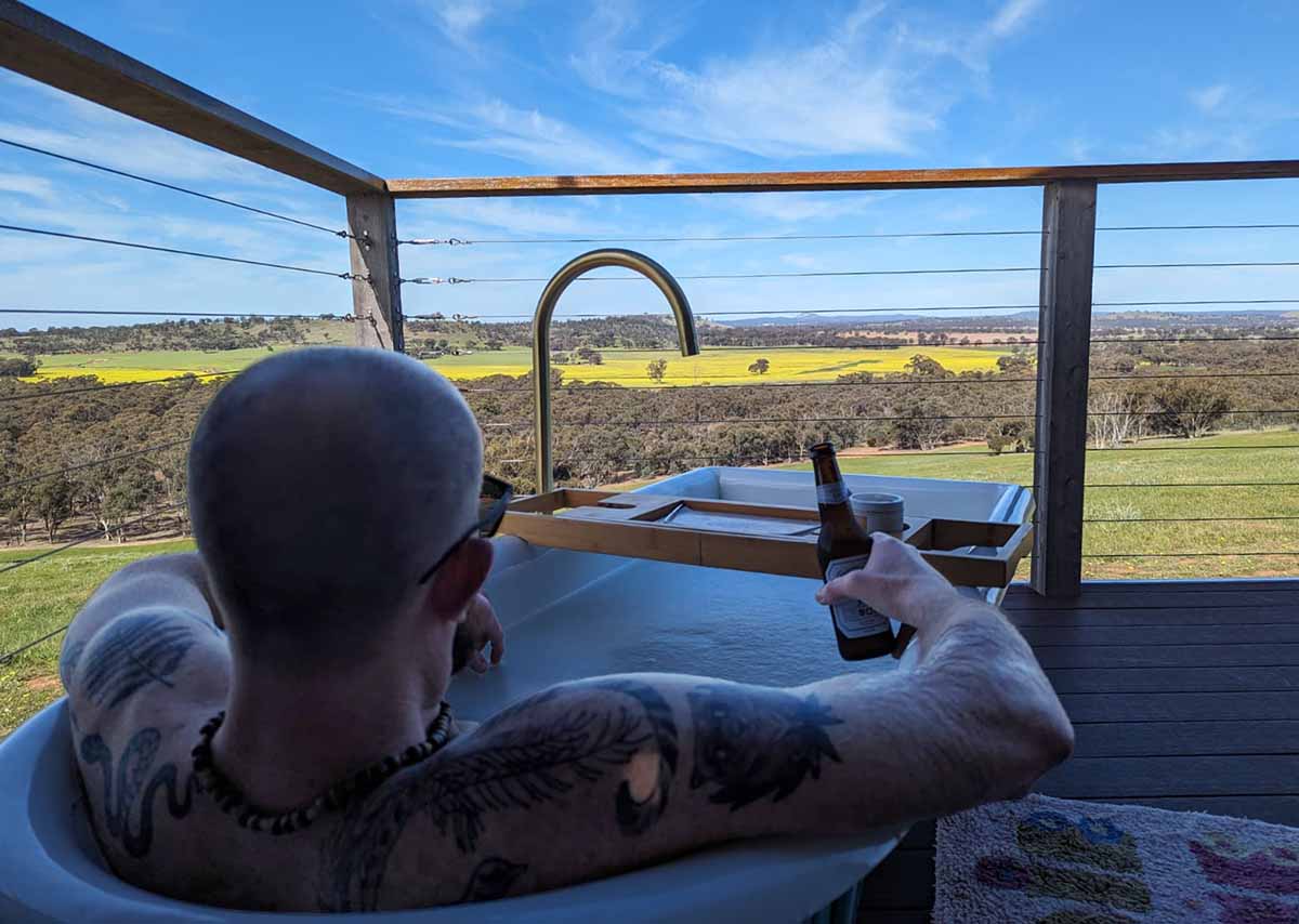 Neil relaxes in the bath on the deck at Kilbirnie Peak, with a beer in hand, looking out at the view